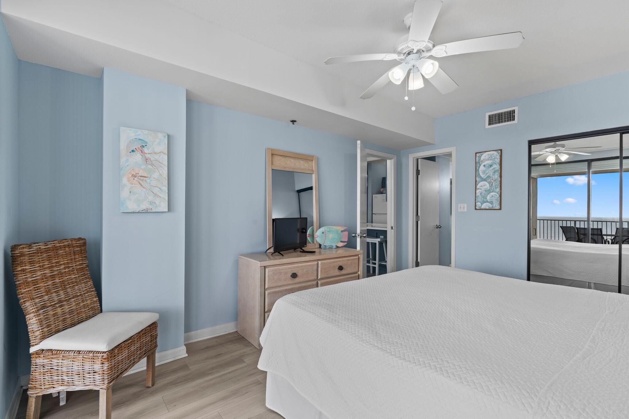 Une chambre à coucher avec un grand lit, un ventilateur de plafond, une commode avec un miroir et des œuvres d’art accrochées aux murs.