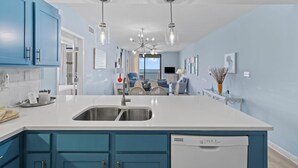 A modern kitchen with blue cabinets, a white countertop, and a built-in dishwasher. - Shoalwater 1005 (Orange Beach)
