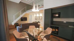 Eine moderne Küche mit Einbauofen und Mikrowelle, ein Essbereich mit Glastisch und gepolsterten Stühlen sowie eine Treppe, die zu einer oberen Ebene führt.