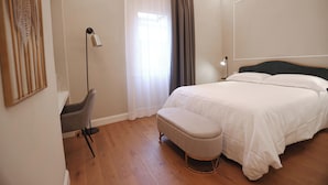 Ein Schlafzimmer mit Bett, Stuhl, Schreibtisch, Lampe und einem Fenster mit Vorhängen.