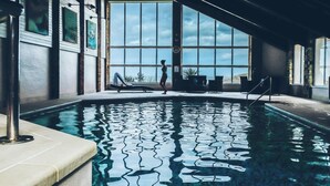Ein Innenpool mit klarem Wasser, großen Fenstern und Liegestühlen.