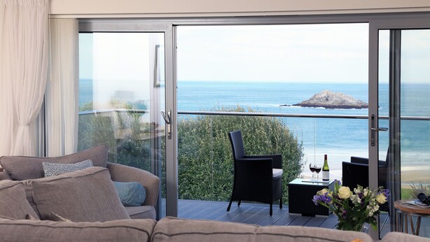 Ein Balkon mit Meerblick, eine Couch, ein Sessel und ein Tisch mit Flasche und Gläsern.