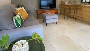 A modern living room with a grey sofa, a small TV, and a dining area with bar stools. - Villa Uma • 50m to Zonte wave • 2Bdr (El Zonte)