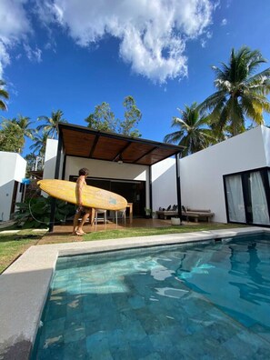 A modern house with a pool, a covered patio, and palm trees.