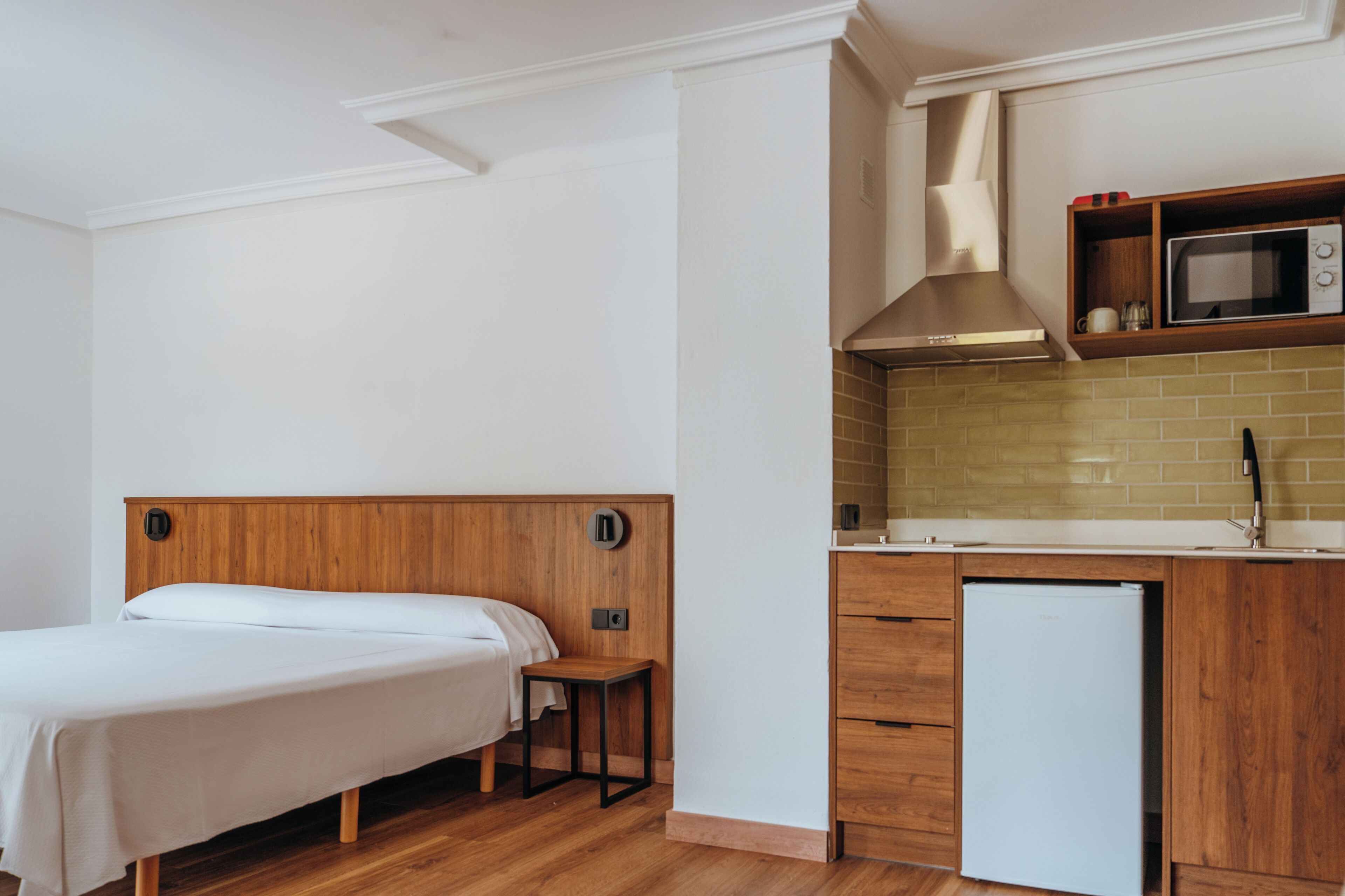 A compact room with a bed, a small table, a microwave, and a refrigerator.