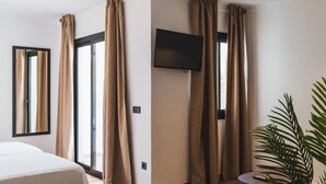 Una habitación de hotel moderna con cama, televisor de pantalla plana y un amplio ventanal con cortinas.