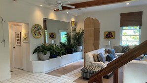 Ein geräumiges Wohnzimmer mit Fliesenboden, einem weißen Sofa, einer Holztreppe und einem Deckenventilator.