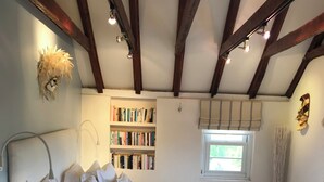 Ein Schlafzimmer mit einem großen Bett, einem Nachttisch, einem Bücherregal und einem Fenster mit Vorhängen.