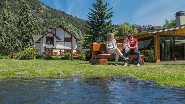 Una familia sentada en un banco junto a una piscina, con una montaña de fondo.