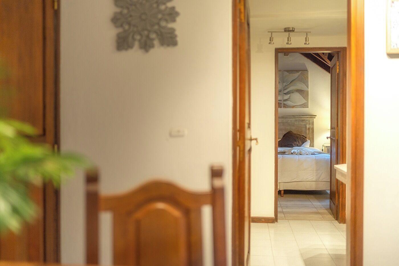 A hallway leading to a bedroom with a bed, a nightstand, and a wall-mounted light fixture.