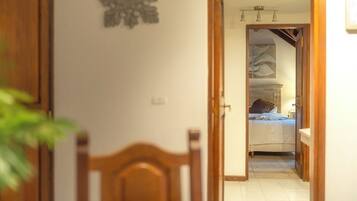 A hallway leading to a bedroom with a bed, a nightstand, and a wall-mounted light fixture.