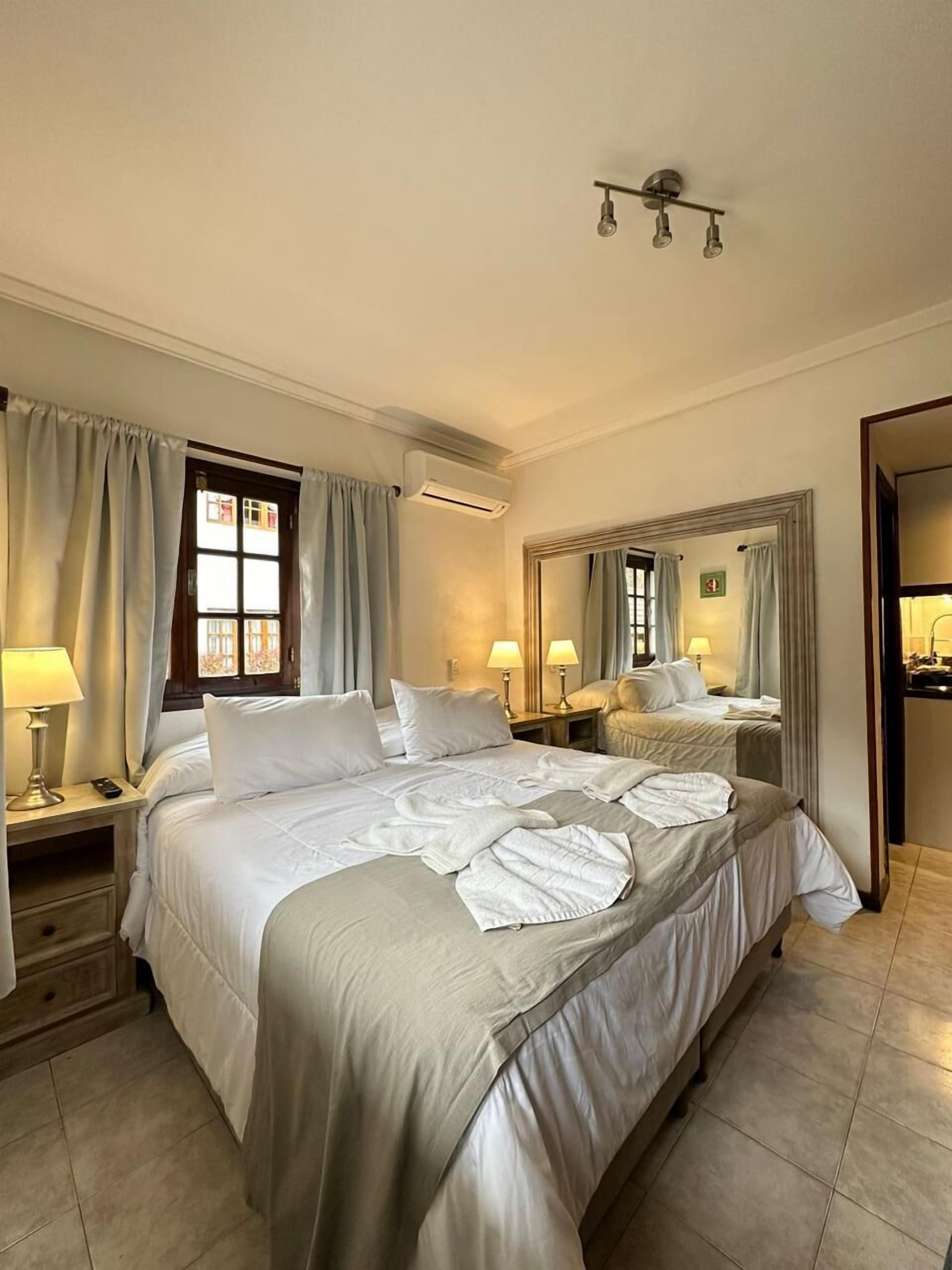 A hotel room with a large bed, two bedside tables with lamps, an air conditioning unit, and a mirror on the wall.
