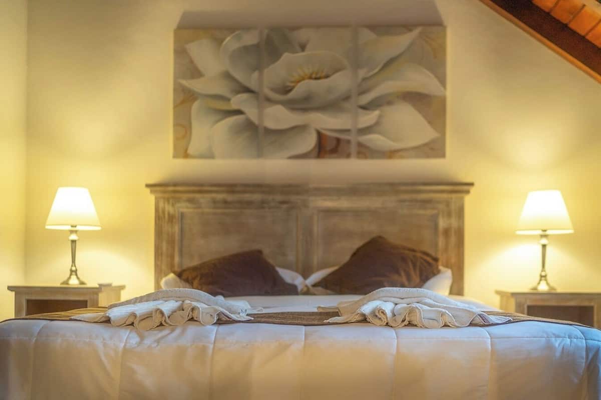 A neatly made bed with a large floral artwork above it, two bedside lamps, and a wooden headboard.
