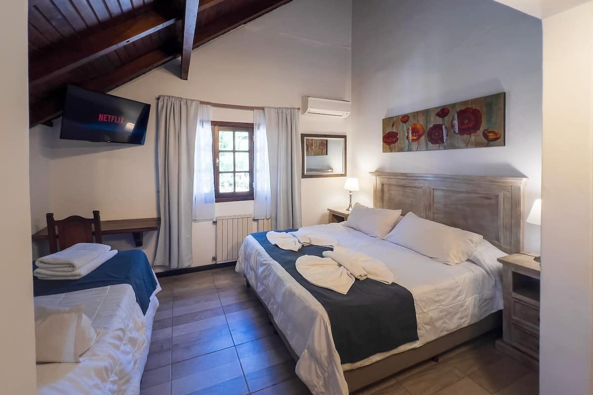 A hotel room with two beds, a television, a window with curtains, a painting, and a lamp.