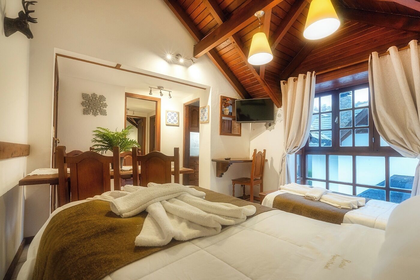Una habitación de hotel acogedora con dos camas, un escritorio, una silla, un televisor y una ventana con cortinas.