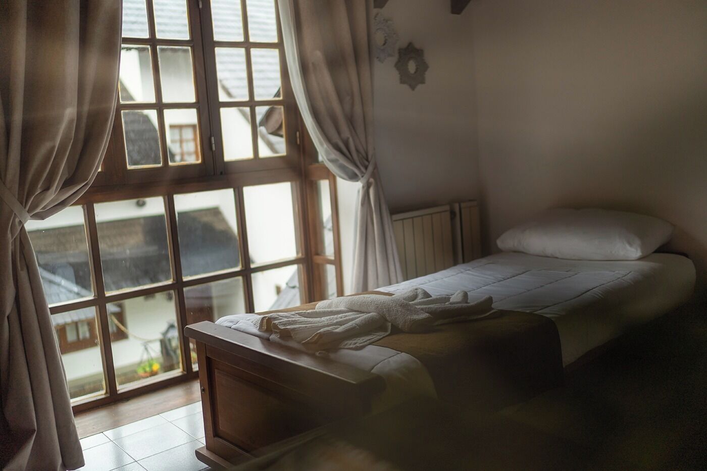 Ein Schlafzimmer mit einem Einzelbett, einem Fenster mit Vorhängen und Blick ins Freie.