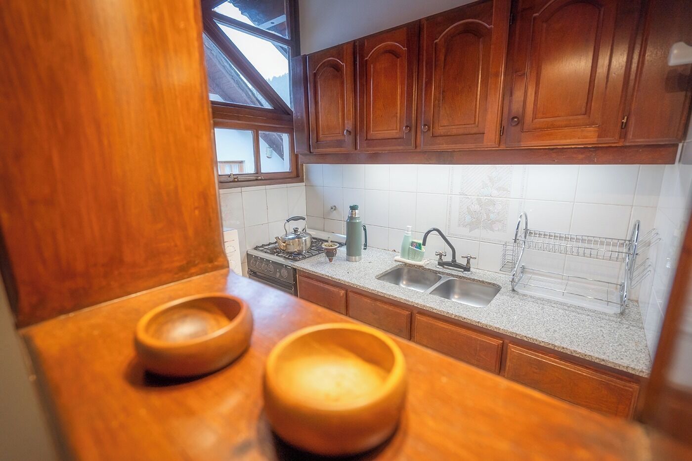 Una cocina con armarios de madera, encimera de granito, pileta doble y ventana sobre la pileta.