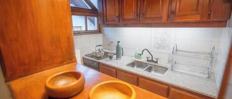 Una cocina con armarios de madera, encimera de granito, pileta doble y ventana sobre la pileta.