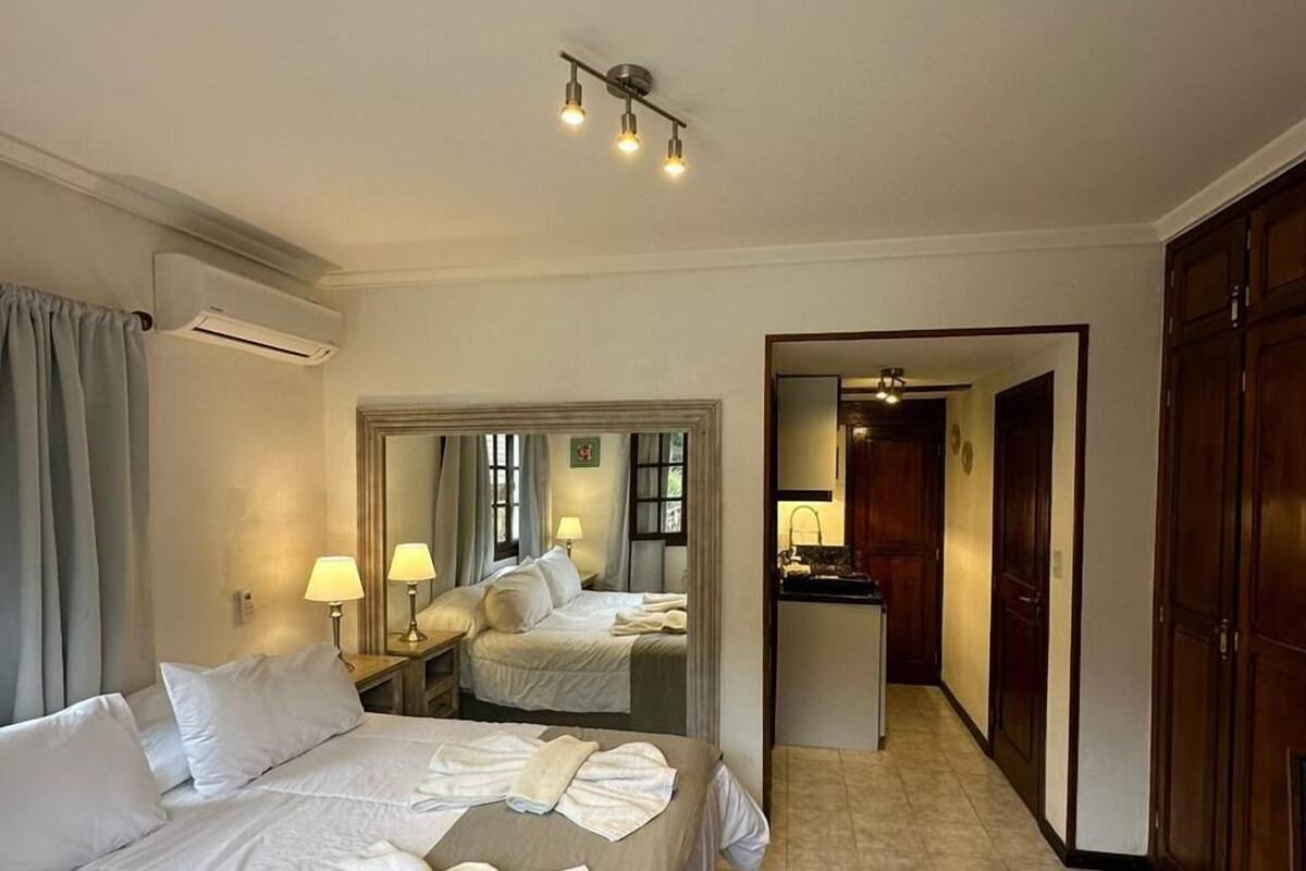A hotel room with a large bed, a desk, a mirror, and a bathroom visible through an open door.