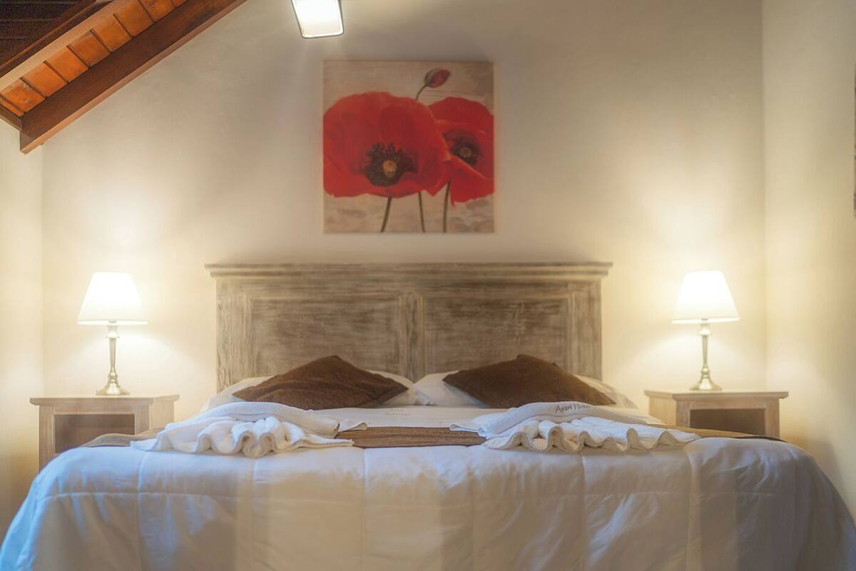 A neatly made bed with white linens and two brown pillows, flanked by two bedside lamps on wooden nightstands.
