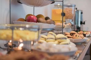 Un buffet proposant une variété d’aliments, notamment des fruits, des pâtisseries et un distributeur de boissons.