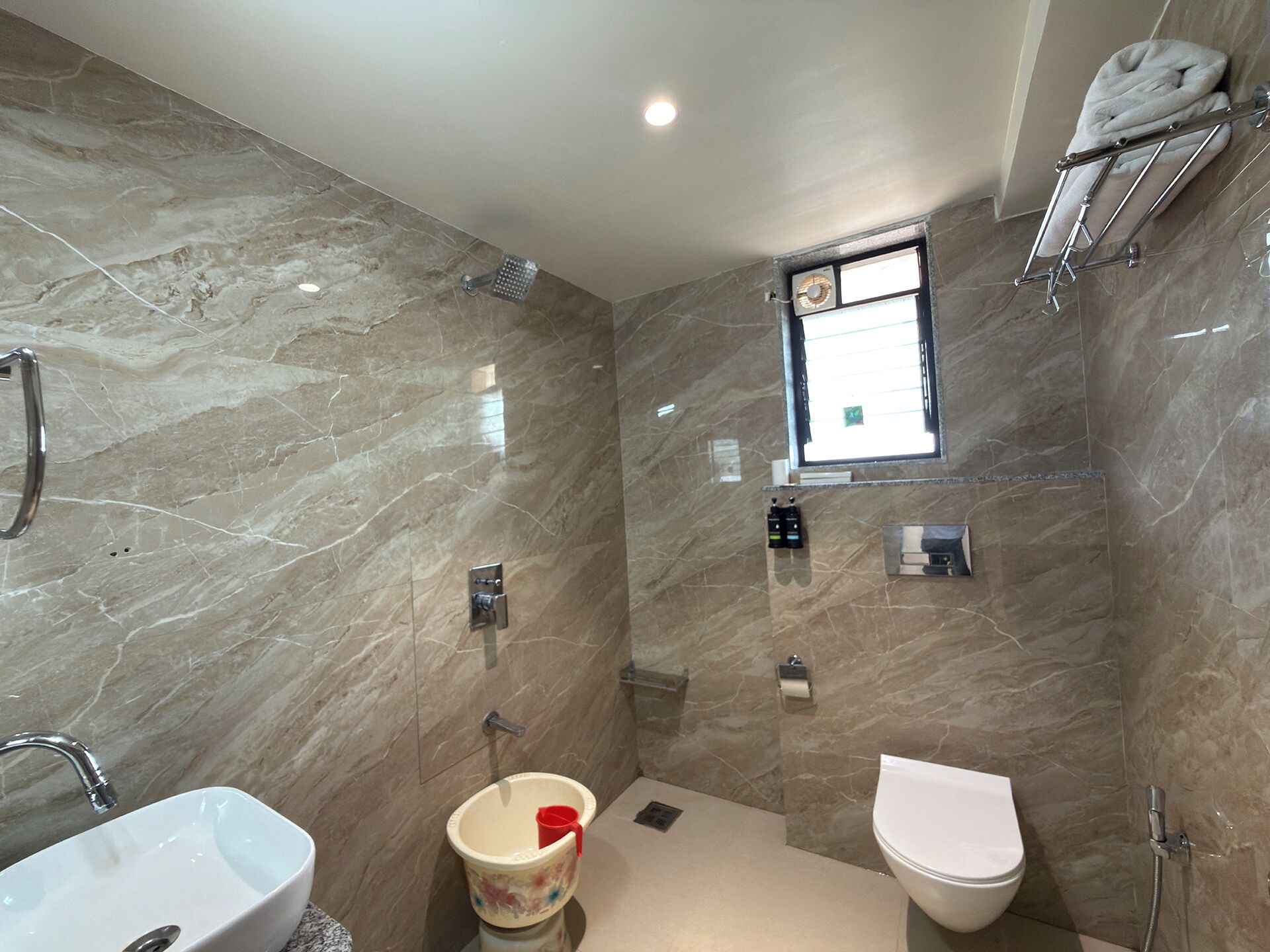 A bathroom with a marble wall, a sink, a toilet, a shower, and a towel rack.