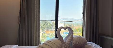 A hotel room with a bed, a purple quilt, and a window with curtains.