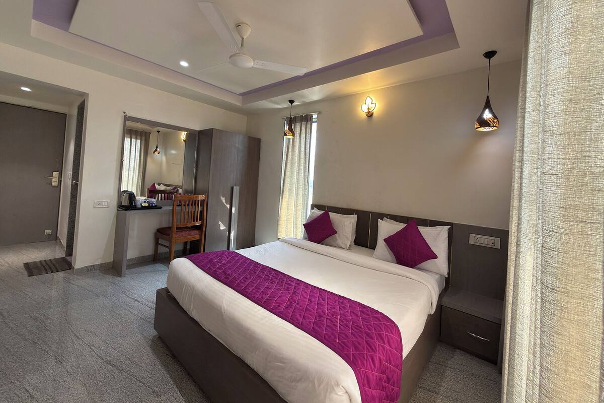 A modern hotel room with a large bed, a desk, a chair, and a ceiling fan.