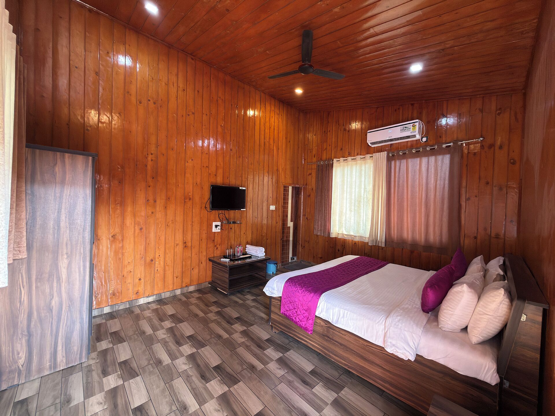 A wooden-paneled room with a bed, a TV, and an air conditioning unit.