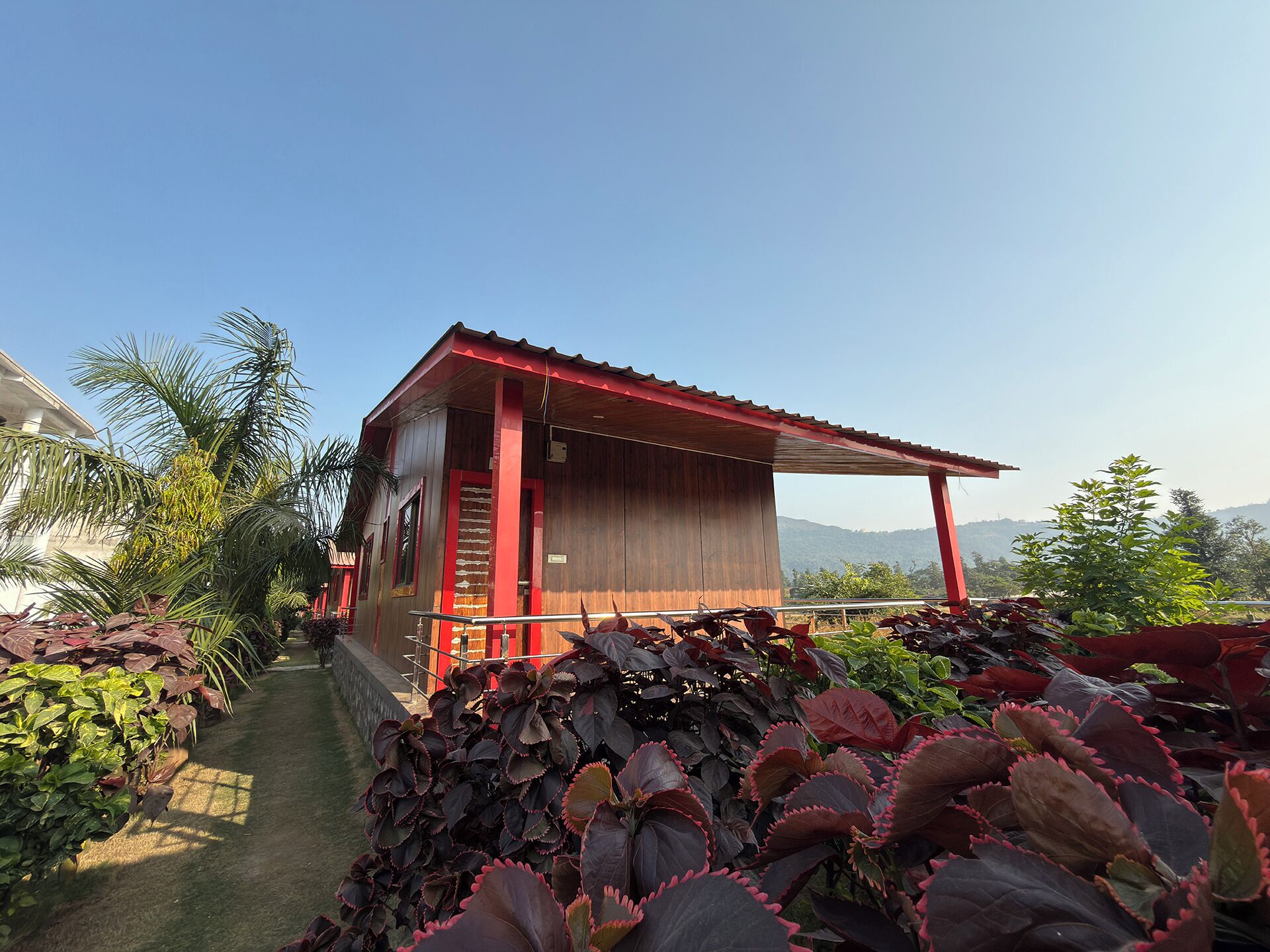 A wooden building with a red roof and a covered porch, surrounded by lush greenery and a clear sky.