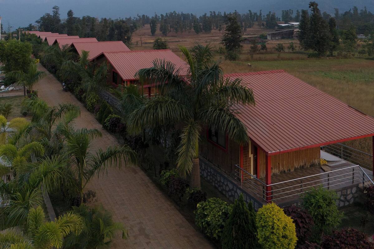 A row of red-roofed buildings with a paved walkway, surrounded by greenery and distant mountains.