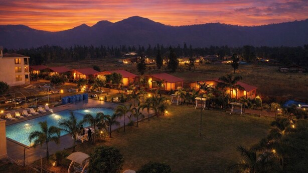 Ein Resort mit mehreren Gebäuden, einem Swimmingpool und Blick auf die Berge bei Sonnenuntergang.