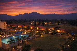 Un complexe hôtelier comprenant plusieurs bâtiments, une piscine et offrant une vue sur les montagnes au coucher du soleil.