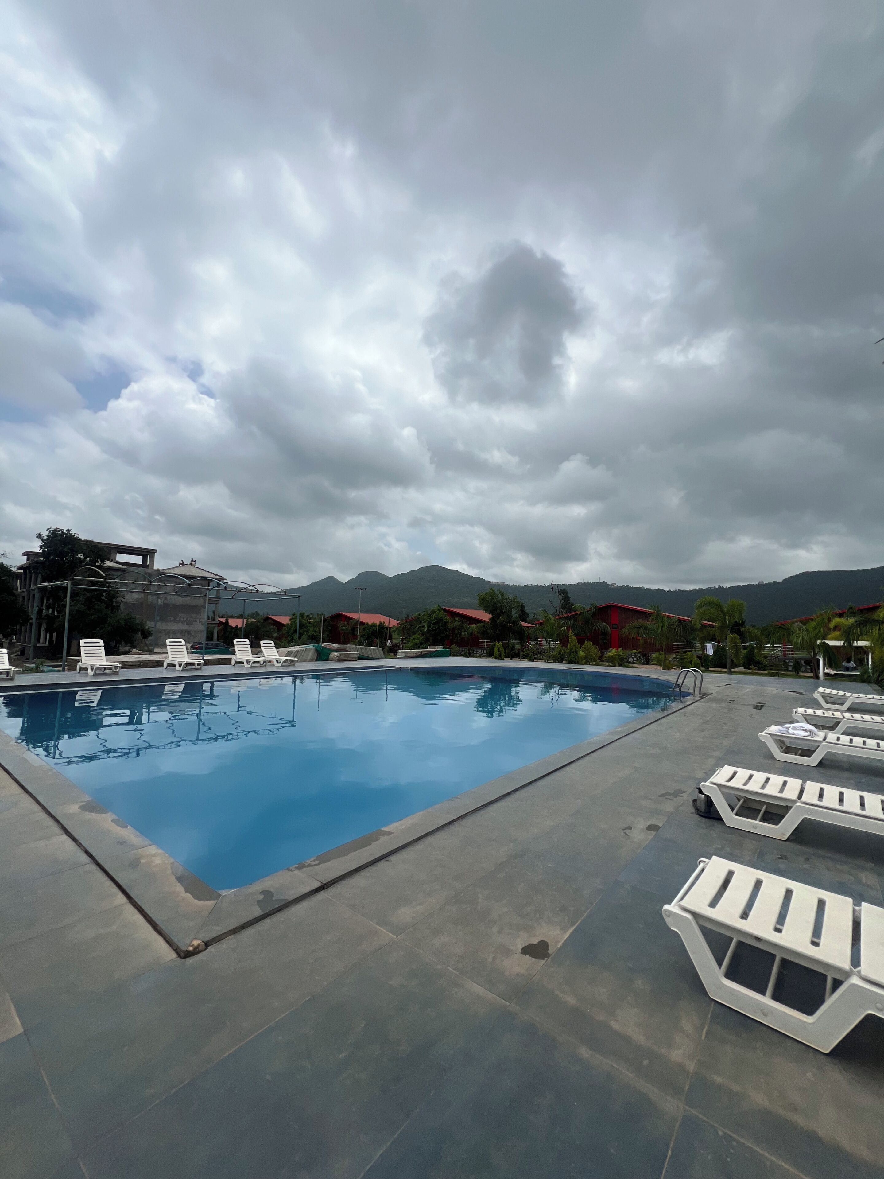 Piscina con sillas de descanso, rodeada de montañas y cielos nublados.