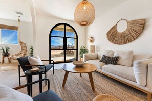 A modern living room with a sofa, a round coffee table, a wicker chair, and a large window with a view of a desert landscape.