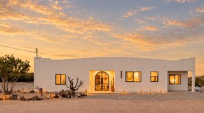 A modern building with a desert landscape, featuring a large arched entrance, multiple windows, and a minimalist design.
