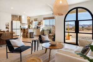 A spacious living area with a large arched window, a kitchen with modern appliances, and a dining area with natural materials. - The Golden Resort | Spa | Pool | Fitness Room (Joshua Tree)