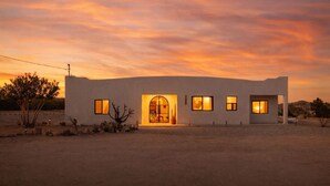 Une maison moderne avec une entrée centrale, de nombreuses fenêtres et un paysage désertique.
