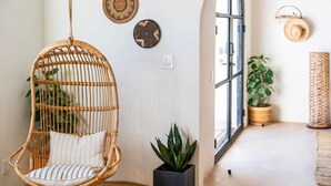 Une chaise en osier, une plante en pot et un panier tressé dans une pièce dotée d’une grande fenêtre et d’une porte.