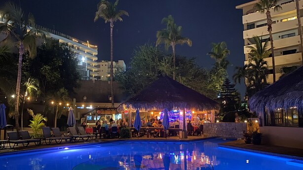 A nighttime pool area with lounge chairs and umbrellas, a bar, and a thatched-roof structure. - C-204 Enjoy Your Vacation In This Exquisite Executive Condominium! (Cabo San Lucas)