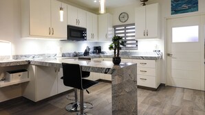 A modern kitchen with white cabinets, a granite countertop, a black bar stool, a microwave, and a clock on the wall. - C-204 Enjoy Your Vacation In This Exquisite Executive Condominium! (Cabo San Lucas)