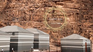 Un camp de luxe avec des tentes à rayures et un paysage rocheux en arrière-plan.