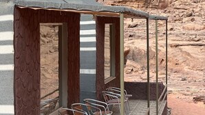 Un espace extérieur aménagé, abrité et doté de chaises en métal et d’un sol carrelé en pierre, le tout adossé à une falaise rocheuse.