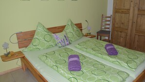 Un lit double avec une parure de lit à motifs verts, deux oreillers, une table de chevet en bois avec une lampe et une armoire en bois.