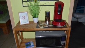 Une table en bois avec un four à micro-ondes, une cafetière rouge, une plante en pot, un panneau « interdiction de fumer » encadré et un petit livre.