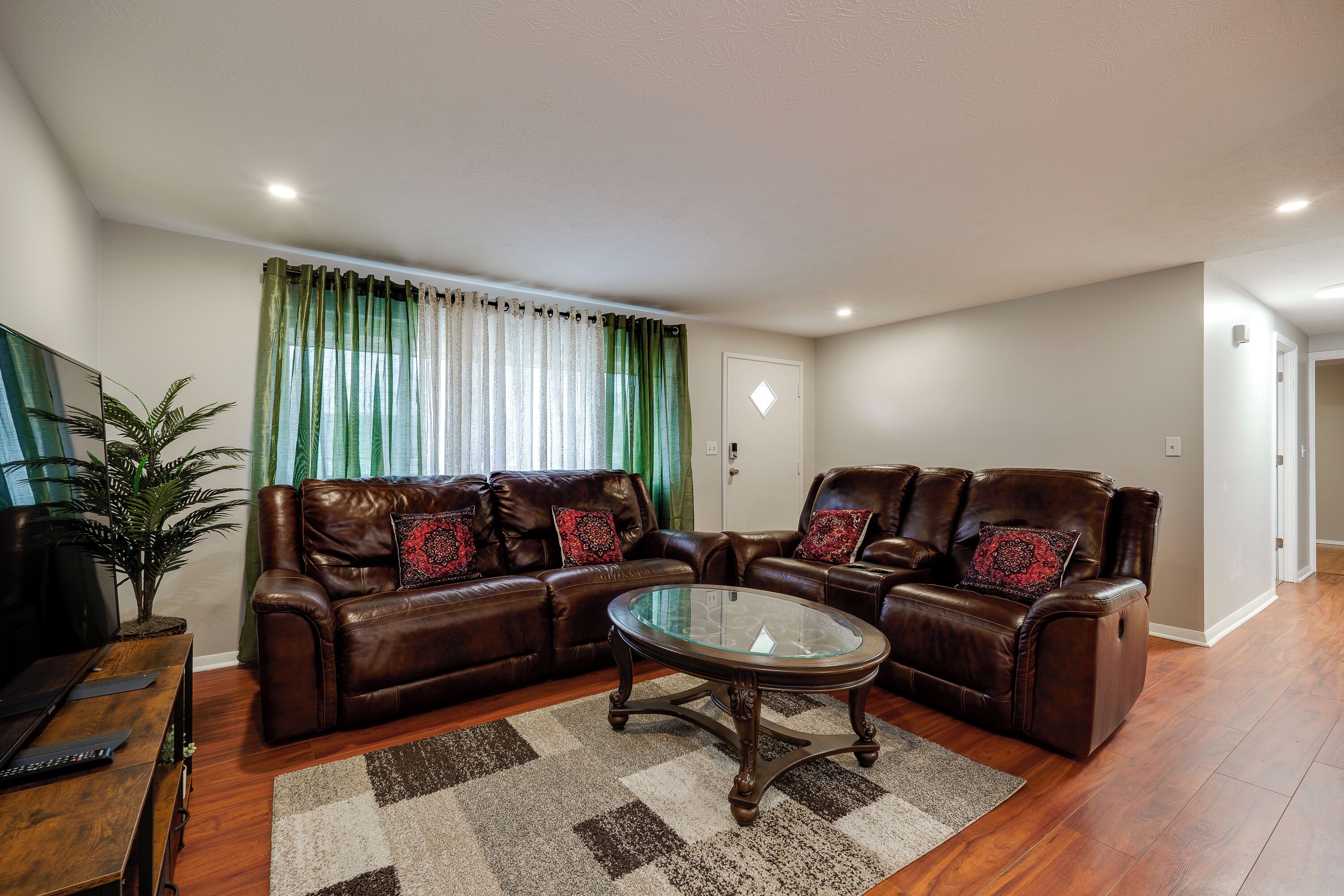 A living room with a brown leather sofa set, a glass coffee table, and a checkered rug.