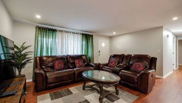 A living room with a brown leather sofa set, a glass coffee table, and a checkered rug.