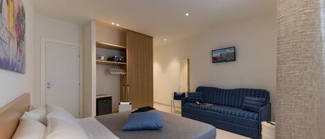 A modern hotel room with a bed, a sofa, a wardrobe, and a small table.