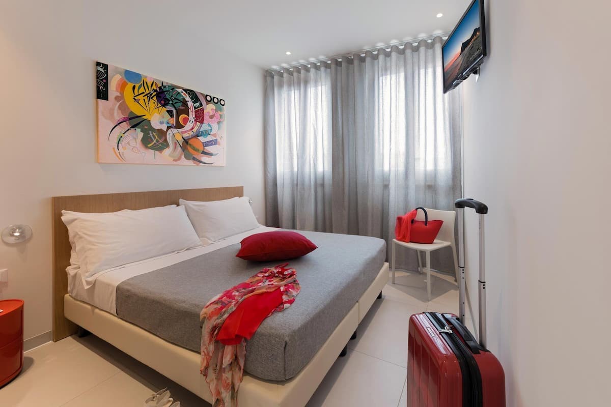 A modern hotel room with a bed, a television, a red suitcase, and a red handbag on a small table.
