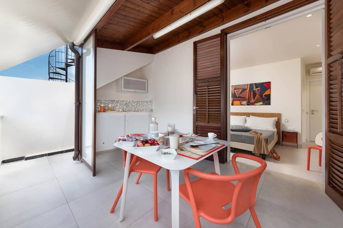 A modern kitchen with a dining area, a staircase, and a bedroom with a bed and artwork.